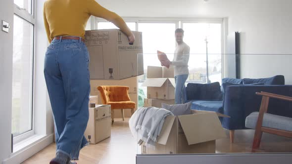 Young Couple Carrying Boxes Into Lounge Of New Home And Unpacking On Moving Day