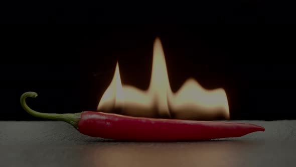 Red cayenne chili pepper on fire on black background