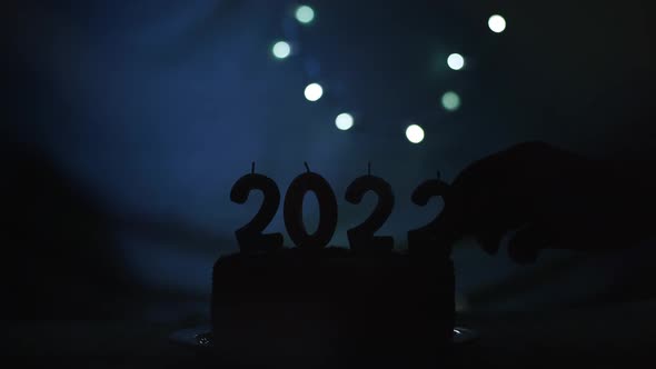 Loading New Year 2022 with Hand Putting and Burning Candle on the Party Cake