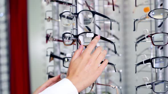Eye glasses on the shelf. Young woman buying new glasses at optician store alt