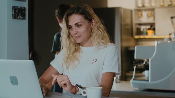 Young blonde woman enjoying taste of coffee serving by barista in coffee shop alt