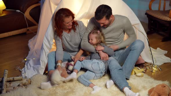 Wide Shot Joyful Father and Mother Playing with Cheerful Little Daughter at Tent in Living Room alt
