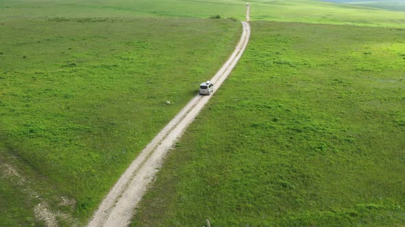 Aerial view on the driving car of the mountain road through the green field