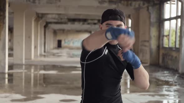 Young Boxer Practicing Boxing Punches Looking at Camera in Abandoned Building alt