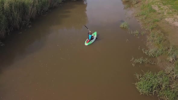 Man kayaking on meandering river, drone follows and pans up to reveal beautiful landscape in the bac alt