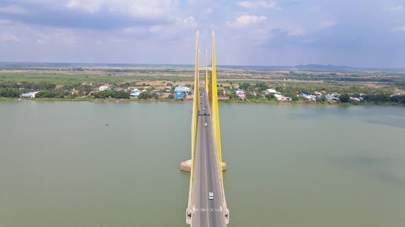 Aerial flyover Neak Loeung Bridge with driving cars crossing calm Mekong River during sunny day. Rur alt