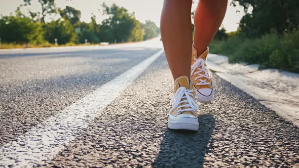 Young Woman's Legs in Yellow Sneakers Moving Along Road alt