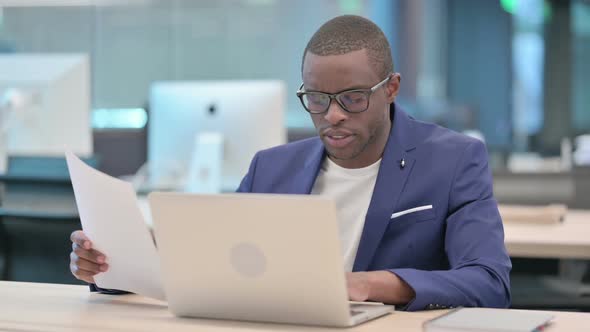 Businessman with Laptop Reading Documents in Office alt