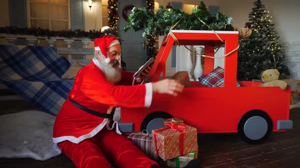 Santa Claus Checking List of Presents on Tablet and Putting Gifts Into Car.