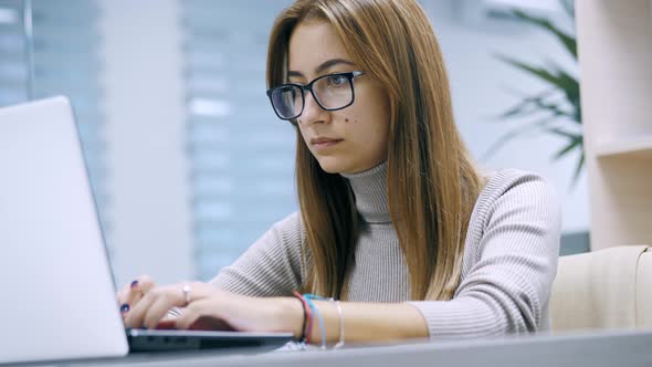 Cute Woman Working at a Laptop with Glasses Typing Text in the Office Employee at Work on the alt