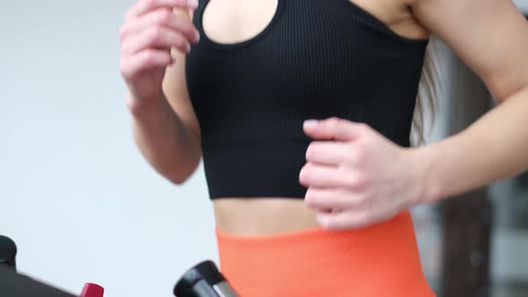 Athletic Girl in the Gym She Runs on a Treadmill Dressed in Orange Sweatpants alt