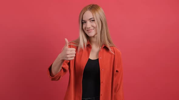 Portrait of Attractive Young Woman Showing a Thumbs Up on Red Background alt