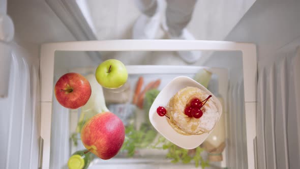 Woman's hands choosing between apples and cake from refrigerator.