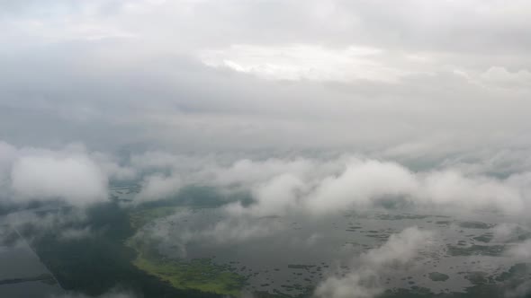 Aerial Top View Drone Flies Through Fluffy Rain Clouds Rolling Over Green Forest By Beautiful Lake alt