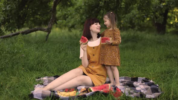 Young Mom with Her Little Cute Daughter on a Picnic in Green Park Eating Watermelon alt