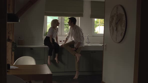 Young Couple in Love Sitting in the Kitchen Flirting and Drinking Wine alt