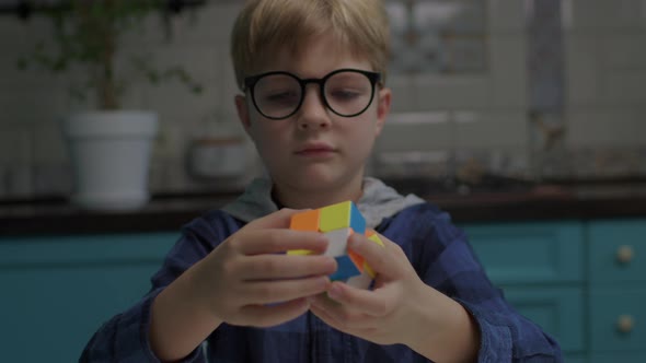 School Boy in Eye Glasses Solving Color Cube Puzzle Holding in Hands alt