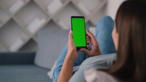 Rear View of Woman in Modern Room Sitting on Couch Using Phone with Green Screen Mockup Chroma Key alt