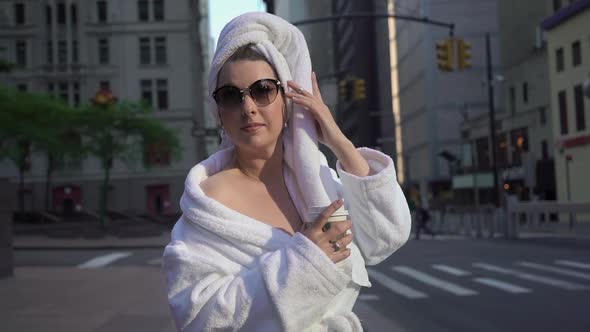 Girl in Bathrobe and Towel on Head in a City Street Drinking Coffee