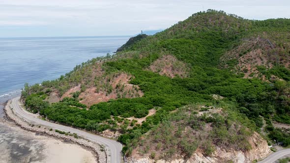 The famous Cristo Rei statue landmark with winding ocean road and green hills in Dili, Timor Leste. alt