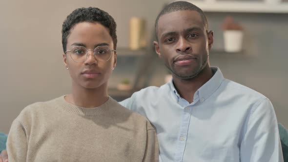 Portrait of Couple Looking at Camera While Sitting on Sofa alt