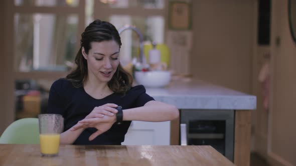 Young adult woman using smart watch at home on kitchen table