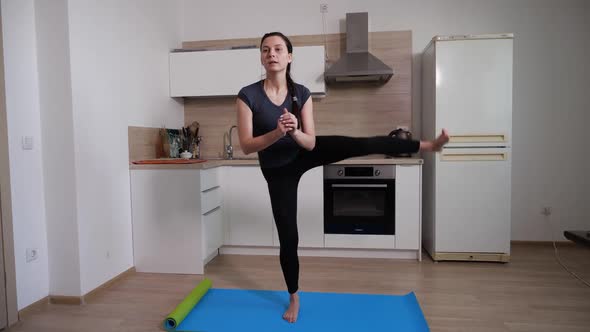 A Brunette Girl Performs an Exercise of Waving Her Feet at Home in the Kitchen