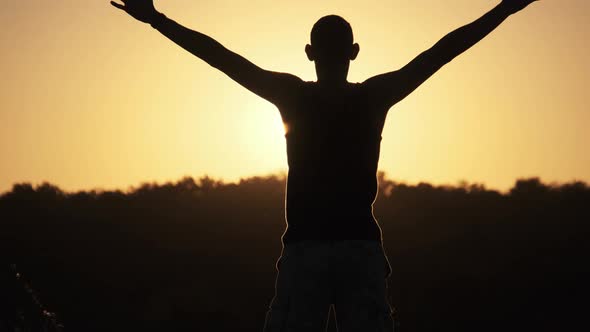Silhouette of Young Man Against Sunset Raising Hands Sides and Up. Slow Motion alt