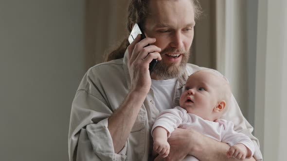 Bearded Caucasian Man Father Adult Multitasking Dad Holding Baby at Home Talking on Phone with alt