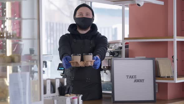 Cheerful Young Barista in Covid19 Face Mask Stretching Disposable Coffee Cups Looking at Camera alt