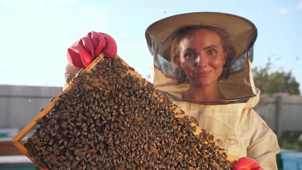 A Girl Beekeeper in a Protective Suit Carries a Frame with Honey From a Bee Hive