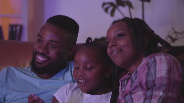 Close Up of Happy African Mother Father and Daughter Watching Tv on Couch at Home alt