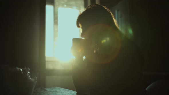 Silhouette of Woman Enjoying Coffee or Tea at Sunset at Home Steam From a Glass Sun Rays Cinematic