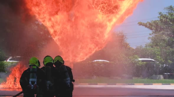 Slow motion group of fireman or fire fighters sit and spray water in front of big fire shoot to sky alt