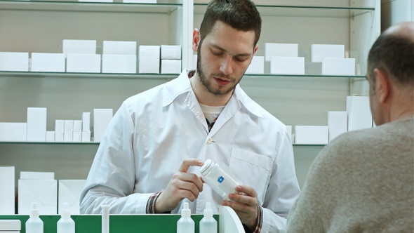 Young Pharmacist Advicing Pills Senior Man Customer at Drugstore