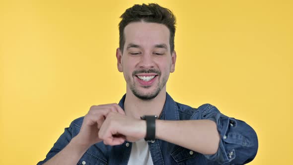 Portrait of Young Man Talking on Smartwatch, Yellow Background alt