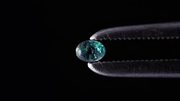 Natural Oval Alexandrite in the Tweezers on the Black Background alt