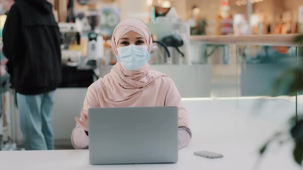 Young Muslim Businesswoman in Hijab in Medical Mask Sits in Public Place Working on Laptop Arab Girl alt