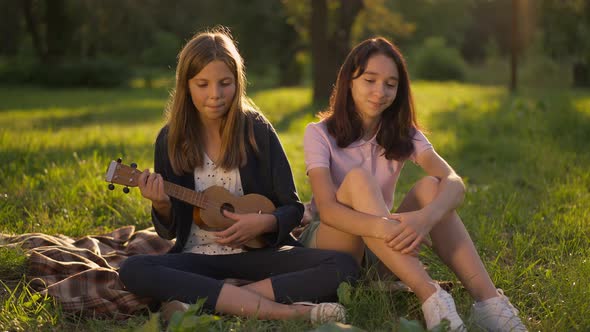 Wide Shot Talented Happy Teenage Girl Singing Playing Ukulele in Sunrays As Friend Listening Smiling alt