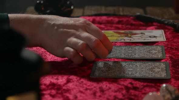 The Fortune Teller's Hand Turns Over Three Tarot Cards Lying on a Burgundy Tablecloth alt
