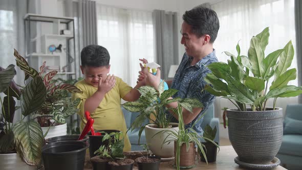Happy Father And Son Taking Care Of Home Plants At Table Indoors alt