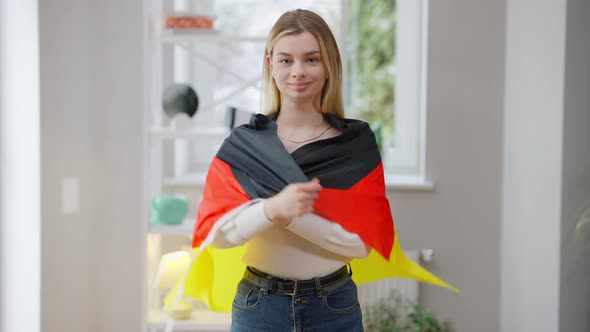 Portrait of Confident Young Woman Wrapping in German Flag Looking at Camera Smiling alt
