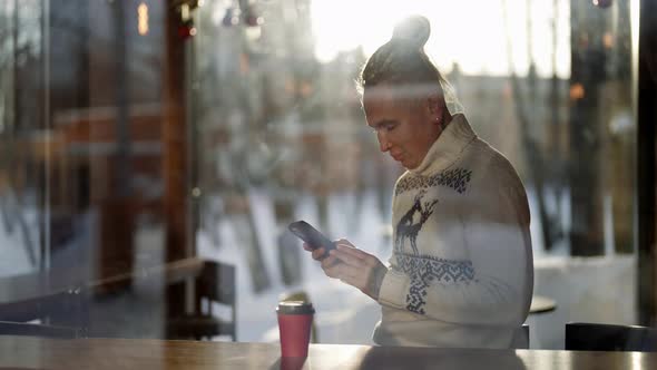 A Homosexual Man is Sitting in a Cafe with a Mobile Phone Behind the Glass alt