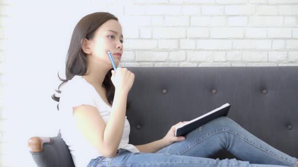 Beautiful asian woman sitting on couch study and learning writing notebook at home. alt