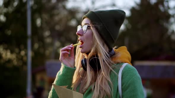 Blonde Girl Eating French Fries Outdoors on Winter Street Dip in Ketchup alt
