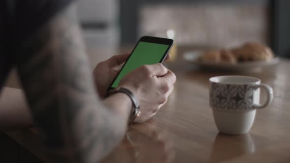 POV young adult male using smartphone at home drinking coffee with greenscreen