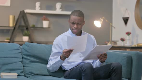 African Man Celebrating Success While Reading Documents on Sofa alt