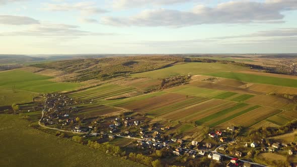 Aerial view of countryside village with small houses among green trees with farm fields  alt