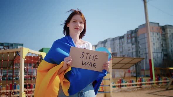 Portrait of a Joyful Ukrainian Woman Holding a Ukrainian Flag and a Sign alt