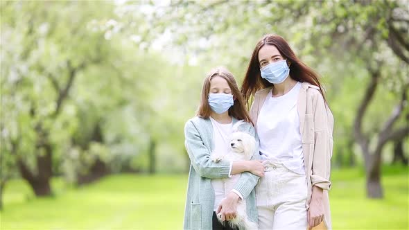 Family of Mother and Daughter in Blooming Cherry Garden in Masks